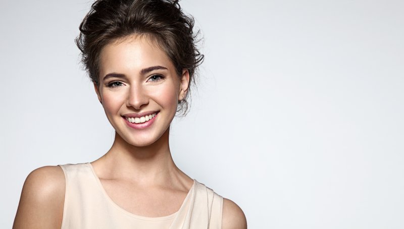 a young woman wearing a cream-colored, sleeveless top and showing off her healthy smile